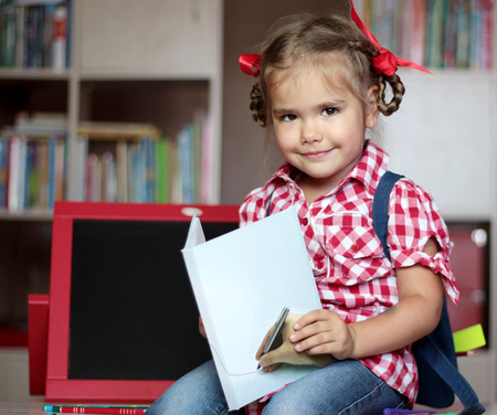 Portrait of cute smiling girl with school implements sitting near the copybook, backpack and colorful pencils, education and back to school conceptの写真素材