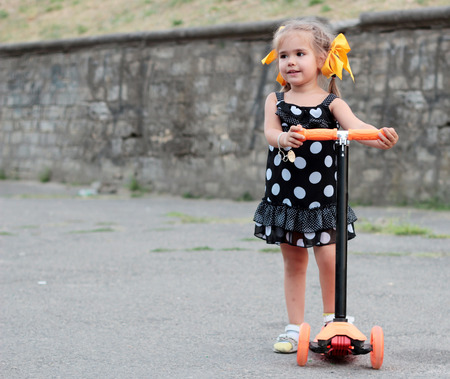 Smiling positive little girl riding the scooter in the park, summer family weekendの写真素材