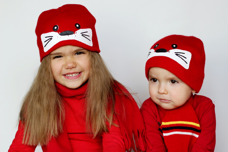 Two little child, boy and girl, wearing red scarves and cute caps over white background, beauty and fashion conceptの写真素材