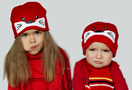 Two little child, boy and girl, wearing red scarves and cute caps over white background, beauty and fashion conceptの写真素材
