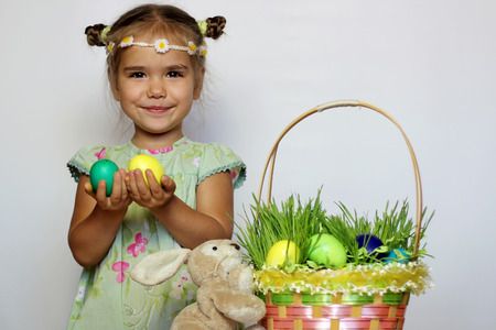 Little smiling girl with bunny and Easter basket with eggs decorated with the grass after egg hunt, happy family holidayの写真素材