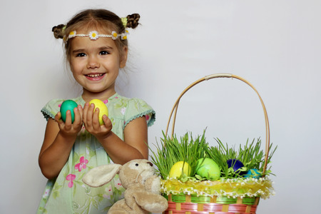 Little smiling girl with bunny and Easter basket with eggs decorated with the grass after egg hunt, happy family holidayの写真素材