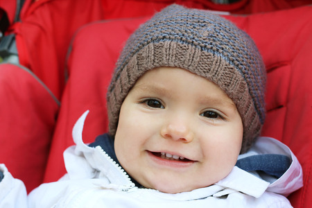 Happy baby in the knitted hat sitting in the stroller, outdoor portraitの写真素材