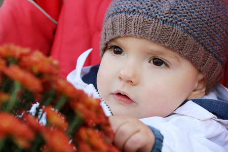 Thoughtful baby in the knitted hat with flowers sitting in the stroller, outdoor portraitの写真素材
