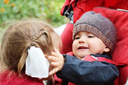Happy baby looking with love and touching a cheek of his elder sister, outdoor portraitの写真素材