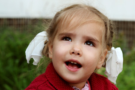 Beautiful little girl with bows smiling and looking up, outdoor portraitの写真素材