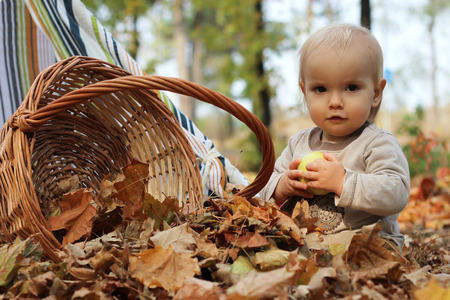 Stylish handsome toddler sitting on the ground near the wicker basket in the autumn parkの写真素材