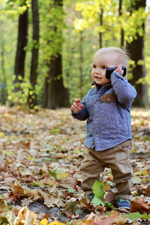 Handsome toddler walking in the autumn park and speaking on the mobile telephoneの写真素材