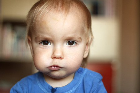 Cute blond baby boy with puffed-out cheek because of sugar candy, indoor portraitの写真素材