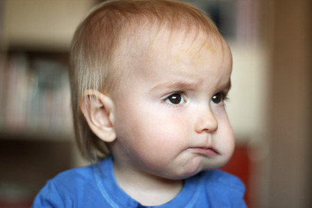 Cute blond baby boy with puffed-out cheek because of sugar candy, indoor portraitの写真素材