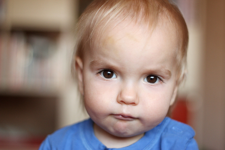 Cute blond baby boy with serious fun grimace and tightened mouth, indoor portraitの写真素材