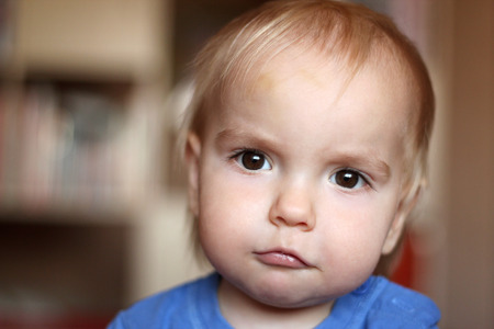 Cute blond baby boy with serious fun grimace and tightened mouth, indoor portraitの写真素材