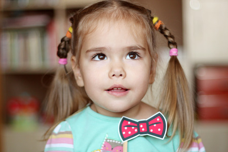 Dreaming pretty toddler girl with bow-tie paper decoration, indoor portraitの写真素材