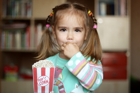Pretty toddler girl for fun eating popcorn paper decoration, indoor portraitの写真素材