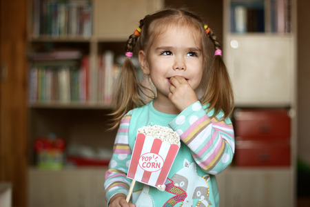 Pretty toddler girl for fun eating popcorn paper decoration, indoor portraitの写真素材