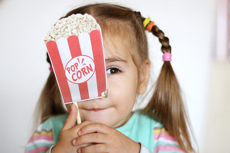 Pretty toddler girl with popcorn paper decoration, indoor portraitの写真素材