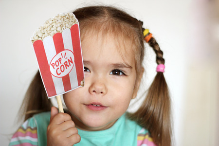 Pretty toddler girl with popcorn paper decoration, indoor portraitの写真素材