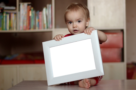 Blond child holding empty blank white frame to put words on a home background, presentation and ad concepts, indoorの写真素材
