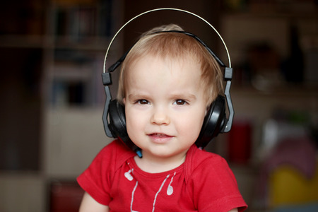 Cute toddler boy listening to music in big head-phones, close-up indoor portraitの写真素材