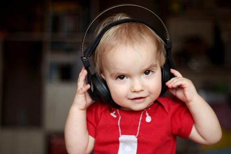 Cute toddler boy listening to music in big head-phones, close-up indoor portraitの写真素材