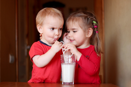 Portrait of cute little girl with handsome toddler boy drinking milk cocktail in a kitchen at home, food and drink concept, healthy food, indoorの写真素材