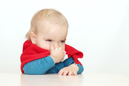 Funny toddler (boy) dressed as a superhero blowing his nose over white background, indoor portrait, superhero conceptの写真素材