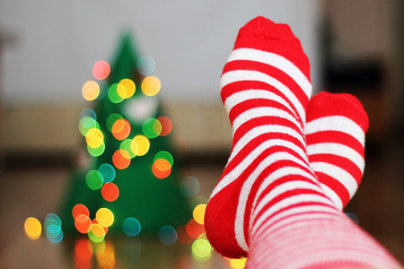 Woman at home. Feet in Christmas socks near blurred Christmas tree. Relaxing and comfort. Winter holiday conceptの写真素材