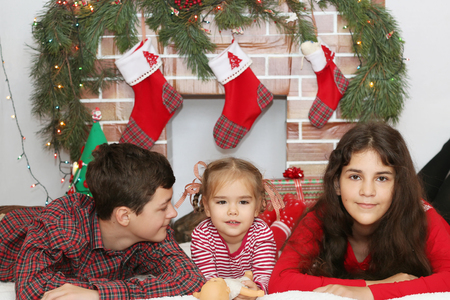 Three smiling children lying near Christmas decorated fireplace, winter holiday conceptの写真素材