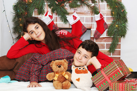 Two smiling children lying near Christmas decorated fireplace, winter holiday family conceptの写真素材