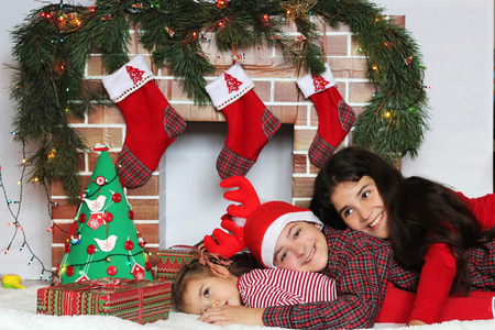Three smiling children lying near Christmas decorated fireplace, winter holiday family conceptの写真素材