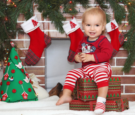 Smiling cute toddler boy sitting on a packed gift and looking for Santa near Christmas decorated fireplace, winter holiday family conceptの写真素材