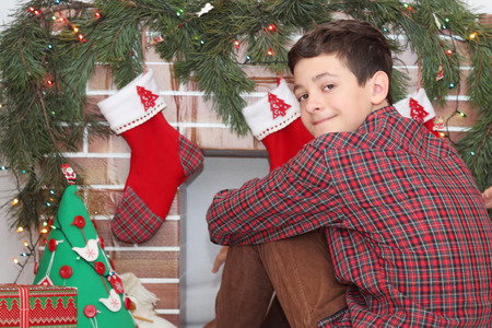 Handsome teenager (boy) sitting near Christmas decorated fireplace, winter holiday family conceptの写真素材