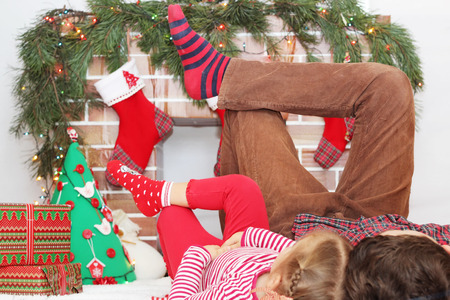Two children lying on their backs with their legs lifted up near Christmas decorated fireplace, winter holiday family conceptの写真素材
