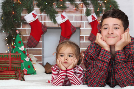 Two children lying supported themselves on the elbow before Christmas decorated fireplace, winter holiday family conceptの写真素材