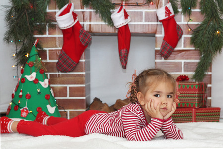 Pretty child girl lying near Christmas decorated fireplace and dreaming about Santa gift, winter holiday family conceptの写真素材