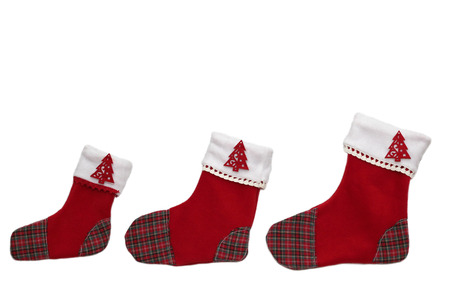 Three red Christmas socks with tree decor for Santa gifts arranged in order from smaller to bigger on white background, winter holidays symbolの写真素材