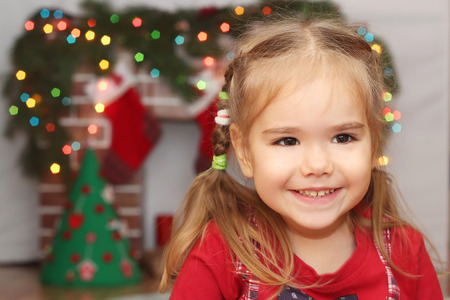 Smiling little girl over blurred Christmas decorated fireplace on background, winter holiday family conceptの写真素材