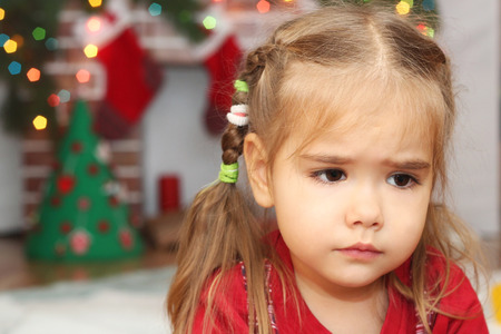 Cute little girl over blurred Christmas decorated fireplace on background, winter holiday family conceptの写真素材