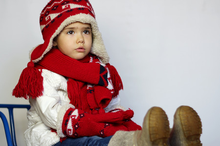 Cute little girl wearing red knitted hat, scarves and mittens on the sled over white background, winter activity conceptの写真素材
