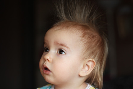 Surprised cute child (boy) with fun face and hair stood on end, indoor portraitの写真素材
