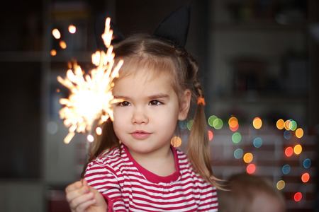 Happy small girl looking with admiration at burning sparkler in her hand over Christmas background