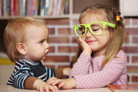 Surprised toddler boy and pretty child girl in funny green eyeglasses sitting at the desk, indoor education conceptの写真素材