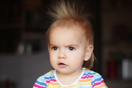 Surprised cute child (boy) with fun face and hair stood on end, indoor portraitの写真素材