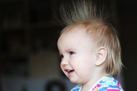 Smiling cute child (boy) with fun face and hair stood on end, indoor portrait, side viewの写真素材