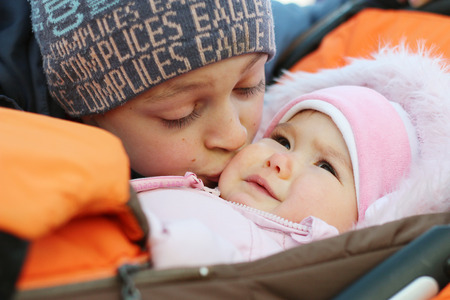 Happy teenager brother kissing baby sister in a stroller, outdoor portraitの写真素材