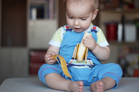 Happy funny toddler boy eating banana fruit, healthy food eating concept, indoor portraitの写真素材