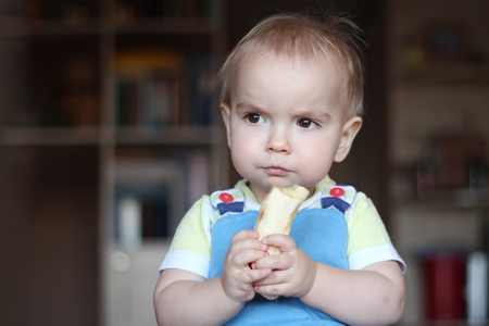 Happy funny toddler boy eating banana fruit, healthy food eating concept, indoor portraitの写真素材