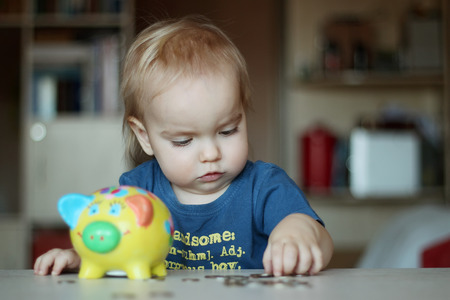 Baby boy inserting a coin into a piggybank, indoor financial conceptの写真素材