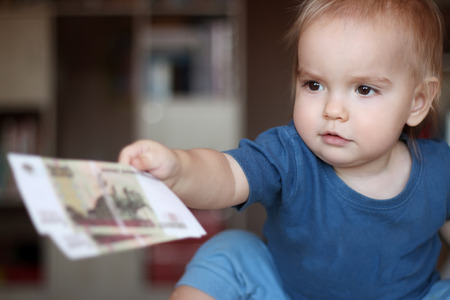Toddler boy reaching out and offering a denomination (money), indoor financial conceptの写真素材