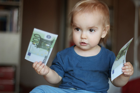 Toddler boy thinking to choose between two denominations (money), indoor financial conceptの写真素材